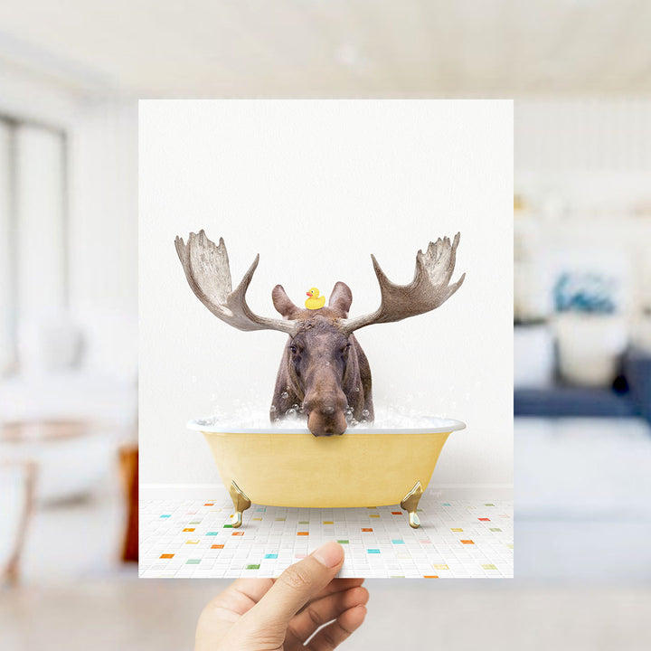 A moose with large antlers is sitting in a yellow bathtub, with a rubber duck perched on its head.
