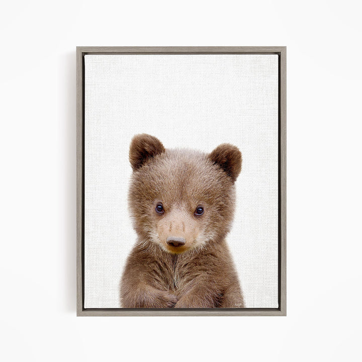 A cute brown bear cub with large eyes and a small nose is the focus of the image.