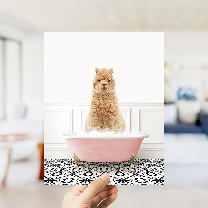 A fluffy brown alpaca sitting in a pink bathtub filled with bubbles, surrounded by a black and white patterned floor.