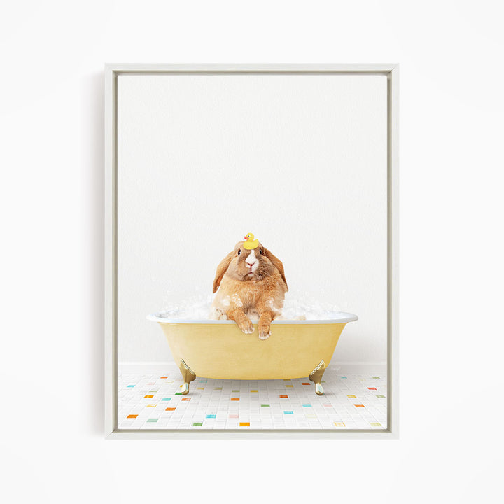 A brown rabbit sitting in a yellow bathtub filled with bubbles, wearing a yellow rubber duck on its head.