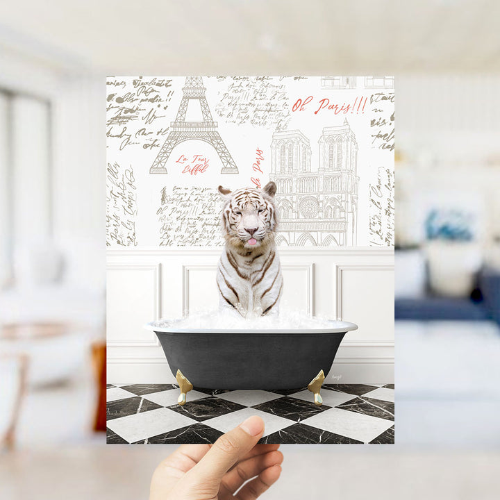 A hand holds up a framed image depicting a tiger sitting in a bathtub filled with water, with the Eiffel Tower and other Parisian landmarks visible in the background.