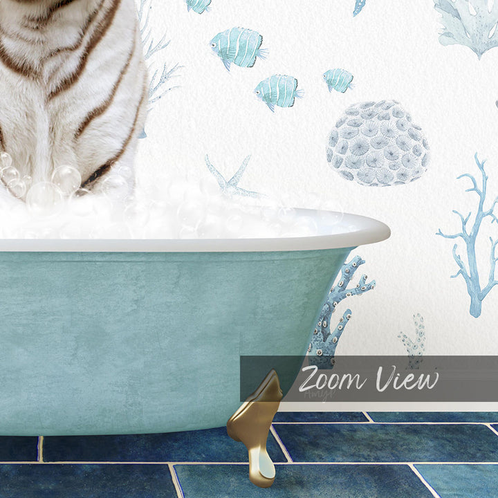A white cat sitting in a blue bathtub filled with bubbles, with a coral and fish mural on the wall behind it.