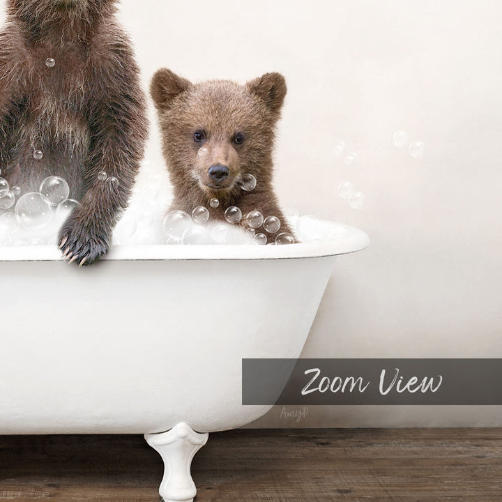 A baby bear sitting in a bathtub filled with bubbles, with a white bathtub and a wooden floor visible in the image.
