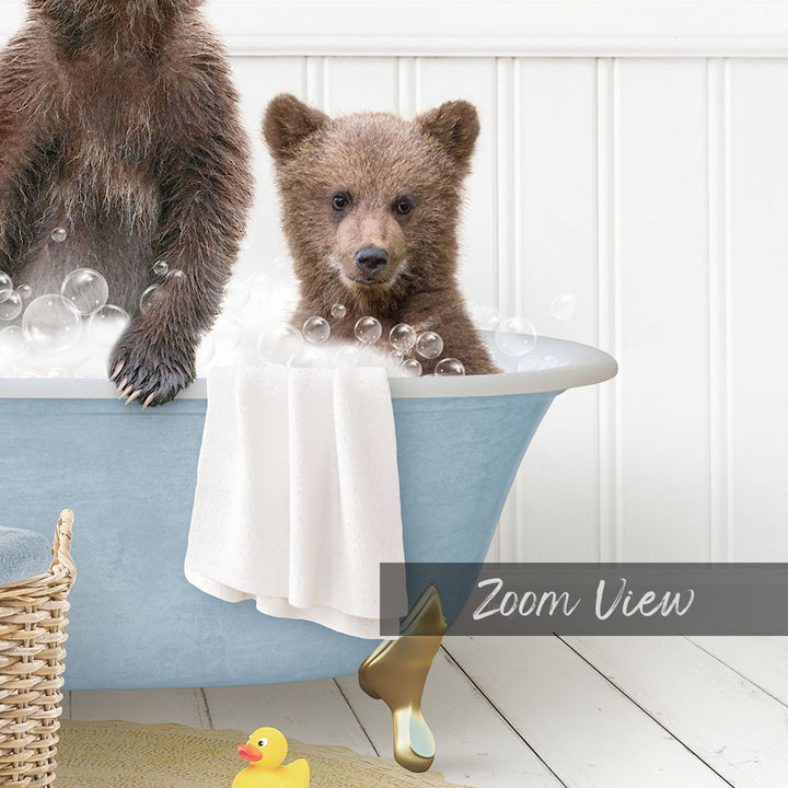 A baby bear sitting in a bathtub filled with bubbles, with a yellow rubber duck nearby.