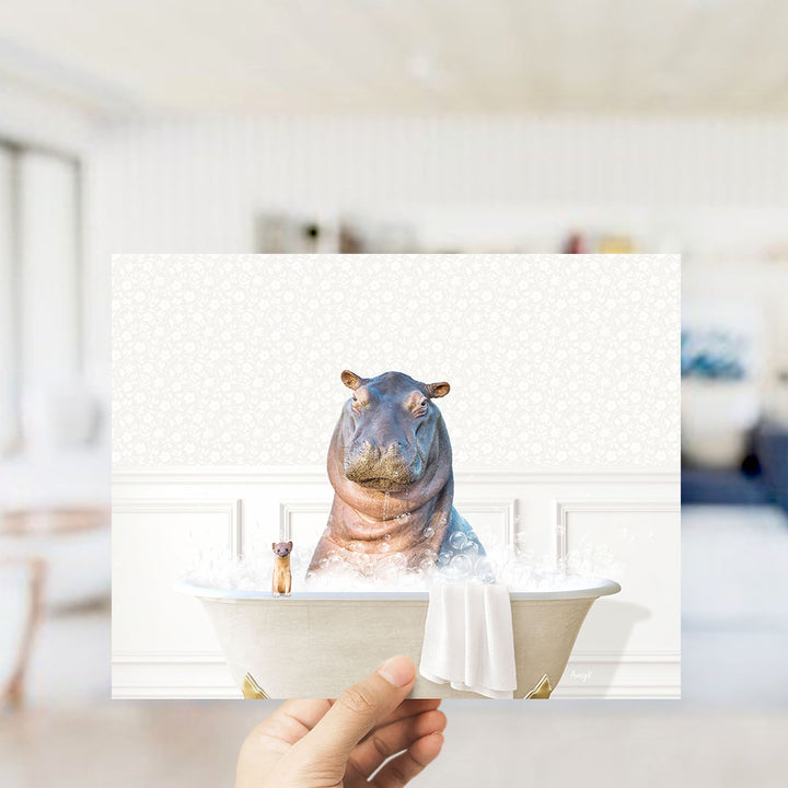 A hand holding a framed image of a hippopotamus sitting in a bathtub, with a towel and a small dog nearby.