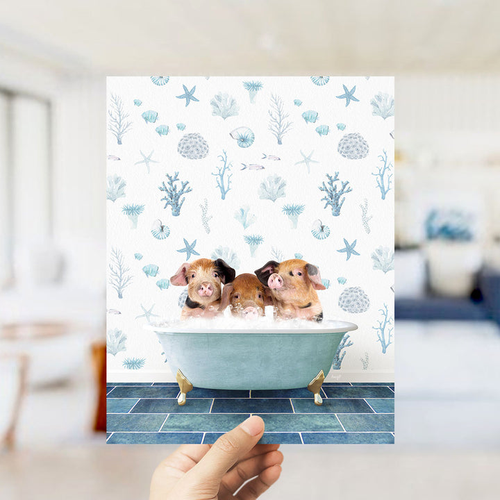 A hand is holding up a printed image of three pigs sitting in a bathtub, surrounded by a pattern of seashells, starfish, and other marine life.