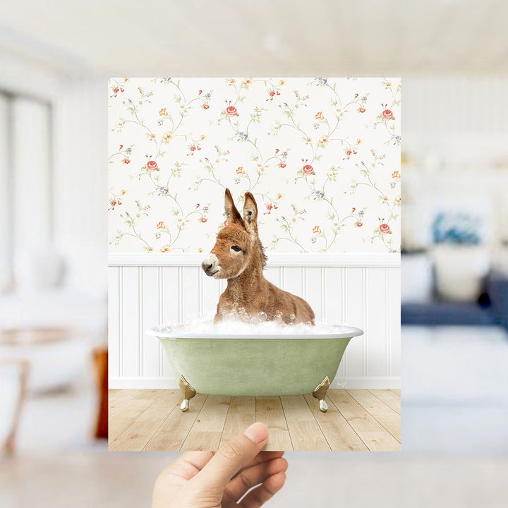 A donkey is sitting in a green bathtub filled with bubbles, surrounded by a floral wallpaper.