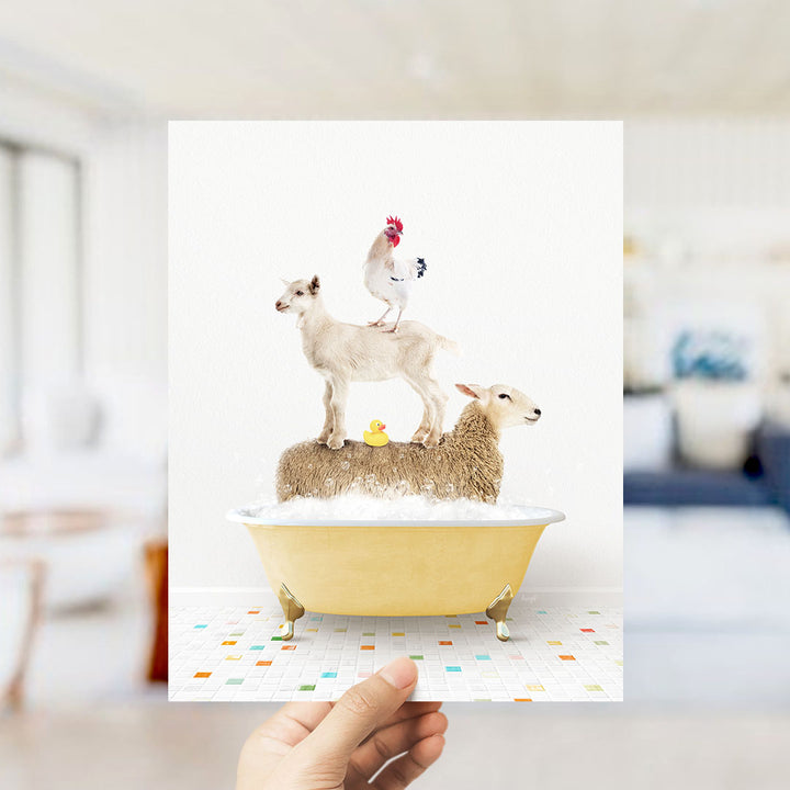 A hand holds up a framed image depicting a goat standing on a sheep's back while a chicken sits on top of a sheep in a bathtub.