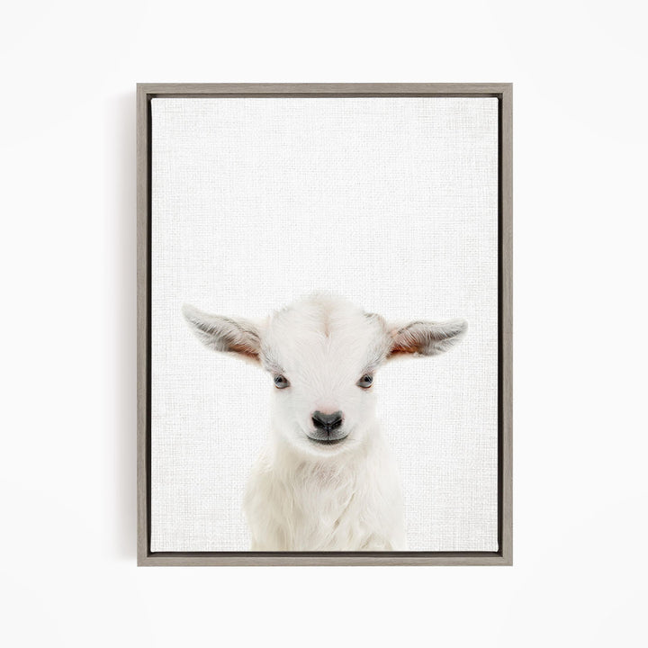 A white goat with large ears is the main subject of the framed print, which is displayed on a white wall.