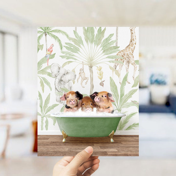 A hand holds up a framed image depicting three pigs sitting in a green bathtub, surrounded by tropical foliage and animals.