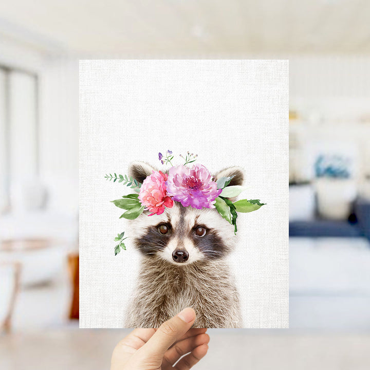 A raccoon wearing a floral crown is being held up against a white background.