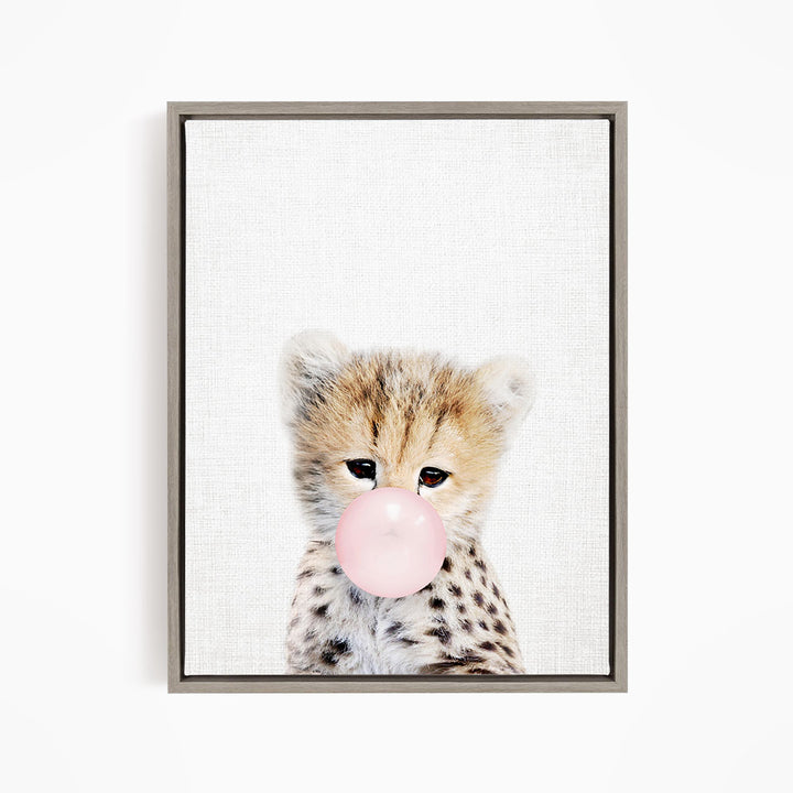 A young cheetah with spotted fur blowing a bubble with a pink bubble gum bubble.