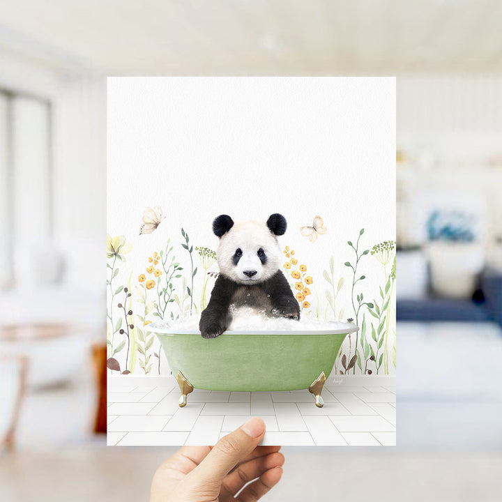 A hand is holding up a framed image of a panda bear sitting in a green bathtub, surrounded by flowers and butterflies.