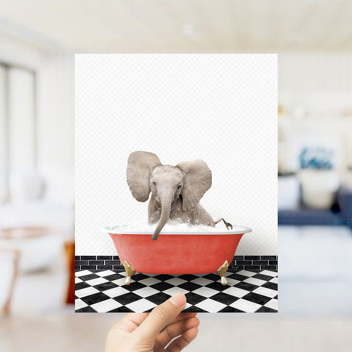 A hand holds up a framed image depicting a baby elephant sitting in a red bathtub filled with water, surrounded by a black and white checkered floor.