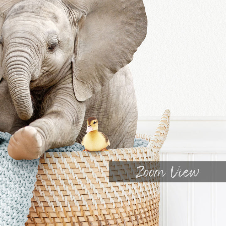 A baby elephant and a duckling are sitting together in a woven basket, with the elephant's trunk resting on the basket.