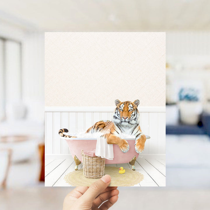 A tiger is sitting in a pink bathtub filled with water, surrounded by a basket and a rubber duck.