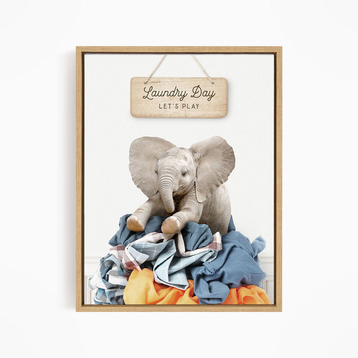 A wooden sign with the text "Laundry Day" hangs above a pile of clothes, with a stuffed elephant sitting on top of the clothes.