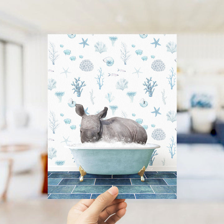 A hand is holding up a print featuring a rhinoceros sitting in a bathtub filled with bubbles, surrounded by a blue and white ocean-themed wallpaper.