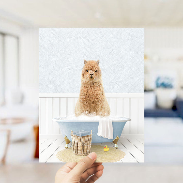 A fluffy brown alpaca sitting in a blue bathtub filled with bubbles, surrounded by a yellow rubber duck and a white towel.