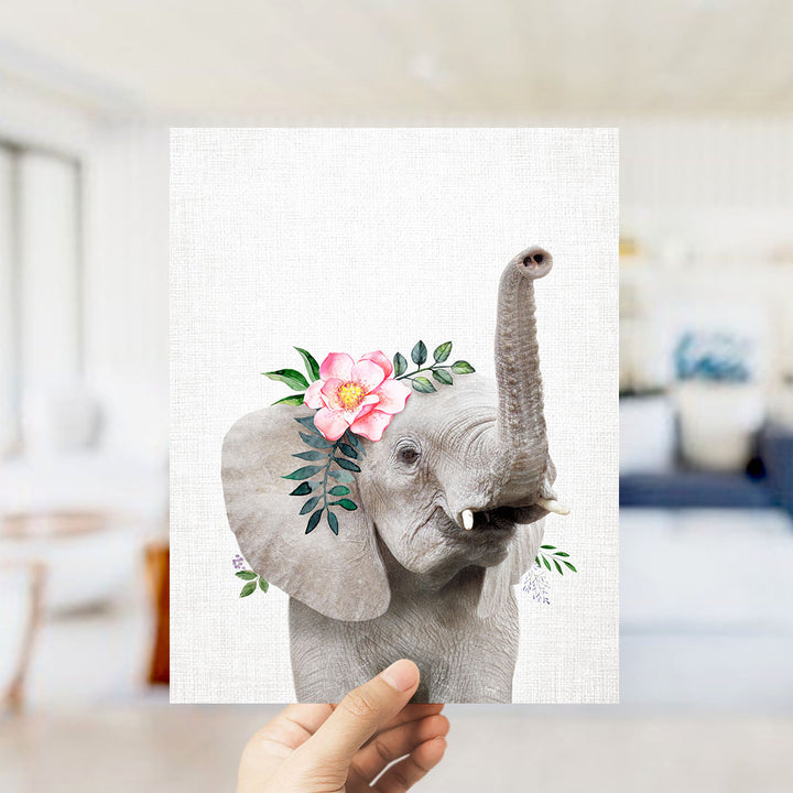 A hand is holding up a framed print of an elephant with a pink flower on its ear.