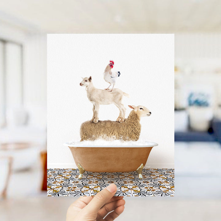 A hand holds up a framed image depicting a goat standing on a sheep's back in a bathtub, with a rooster perched on top of the sheep.