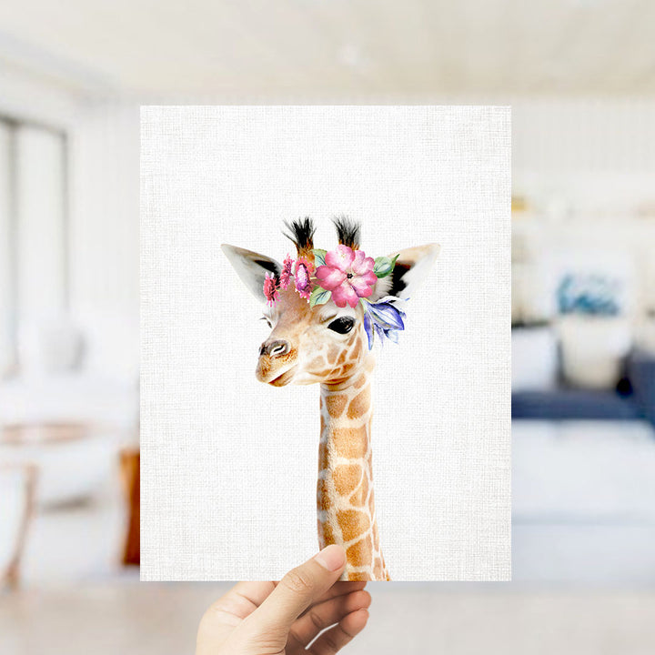 A hand is holding up a framed print of a giraffe wearing a flower crown.