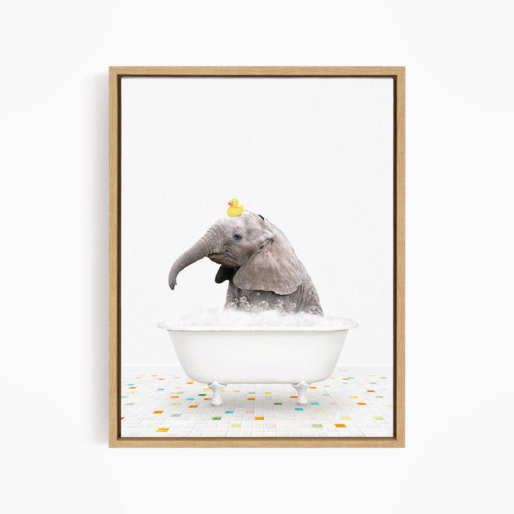 A baby elephant is sitting in a white bathtub filled with bubbles, with a yellow rubber duck perched on its head.