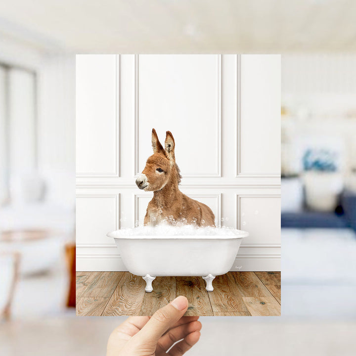 A donkey sitting in a white bathtub filled with bubbles, with a blurred background suggesting a bathroom setting.