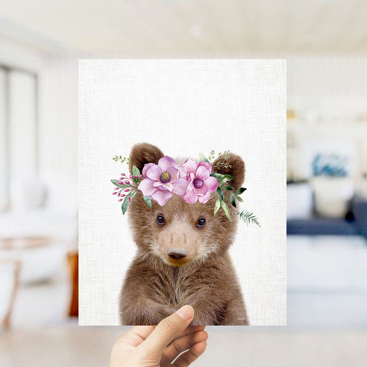 A hand is holding up a framed print of a cute bear wearing a floral crown.