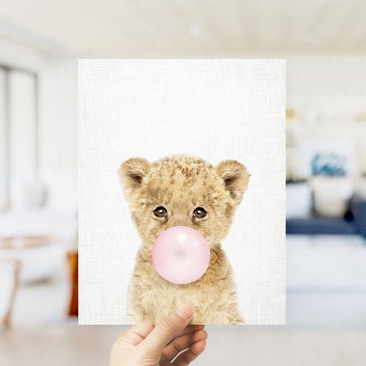 A hand is holding up a framed print of a cute, fluffy animal blowing a bubble with a pink bubble gum bubble.