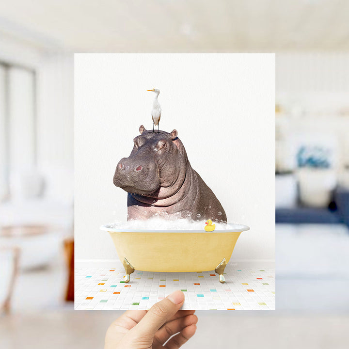 A hand holds up a collage of images depicting a hippopotamus sitting in a bathtub, with a bird perched on its head.