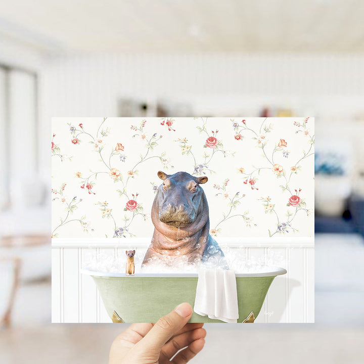 A hand holding a framed image of a hippopotamus sitting in a bathtub, surrounded by a floral pattern.