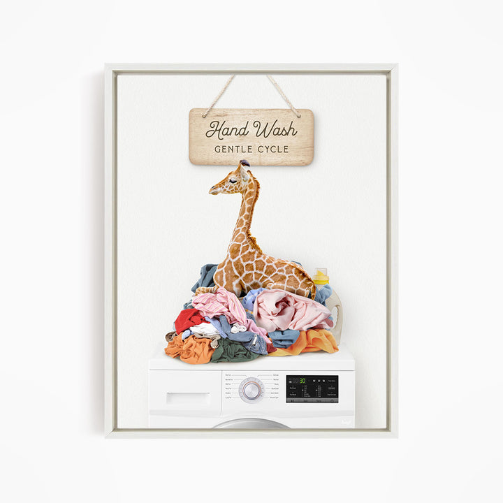 A giraffe sitting on a pile of laundry, with a sign above that says "Hand Wash Gentle Cycle".
