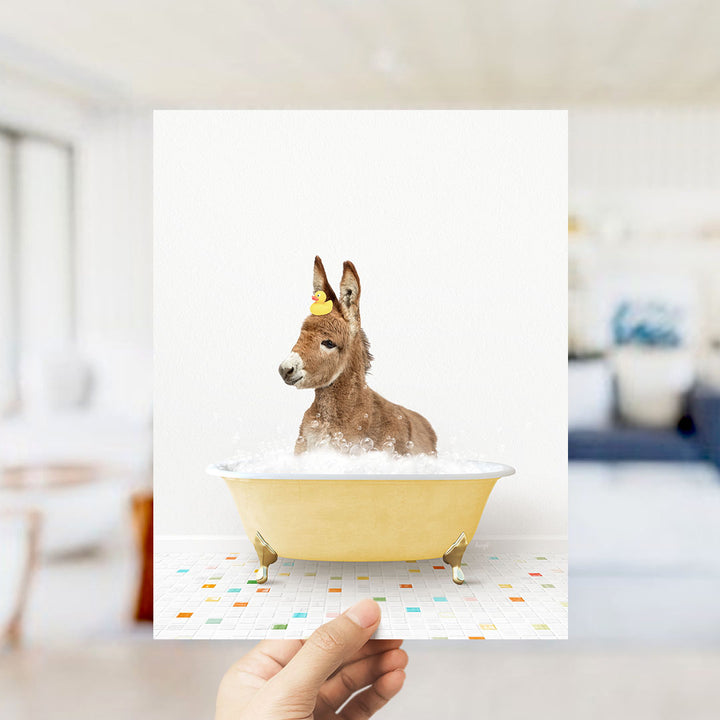 A donkey is sitting in a yellow bathtub filled with bubbles, wearing a yellow rubber duck hat.