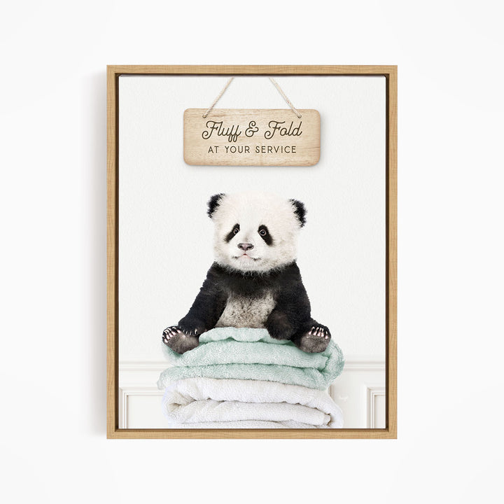 A panda bear sitting on a stack of towels, with a wooden sign above that says "Fuffy & Fold at your service".