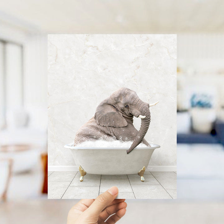 A hand holds up a framed image of a gray elephant sitting in a white bathtub filled with bubbles, creating a whimsical and playful scene.