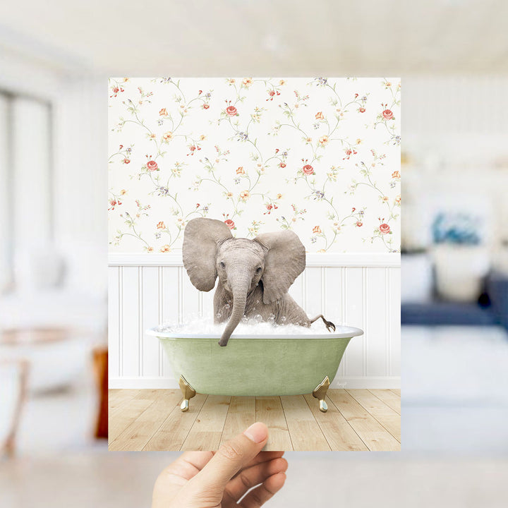 A small elephant sitting in a green bathtub filled with water, surrounded by a floral patterned wall.