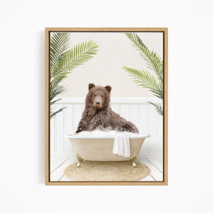 A brown bear sitting in a white bathtub filled with water, surrounded by green palm leaves.