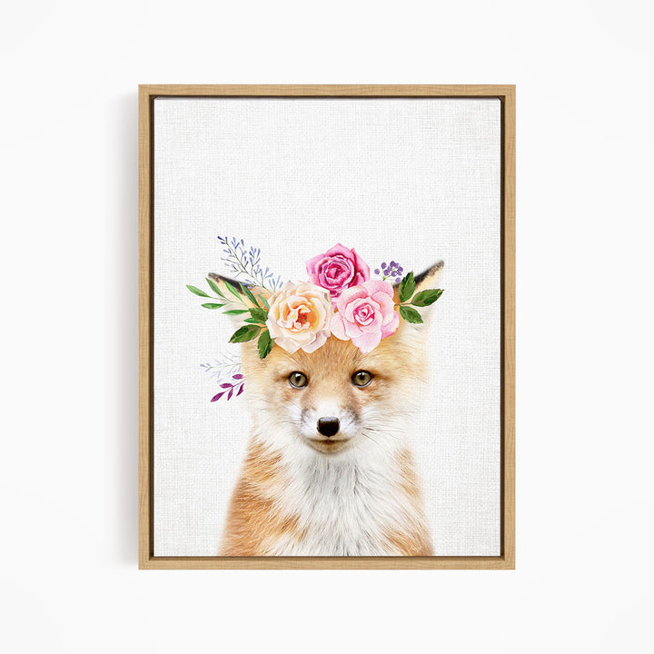 A framed print of a fox wearing a floral crown of pink and orange roses and greenery.