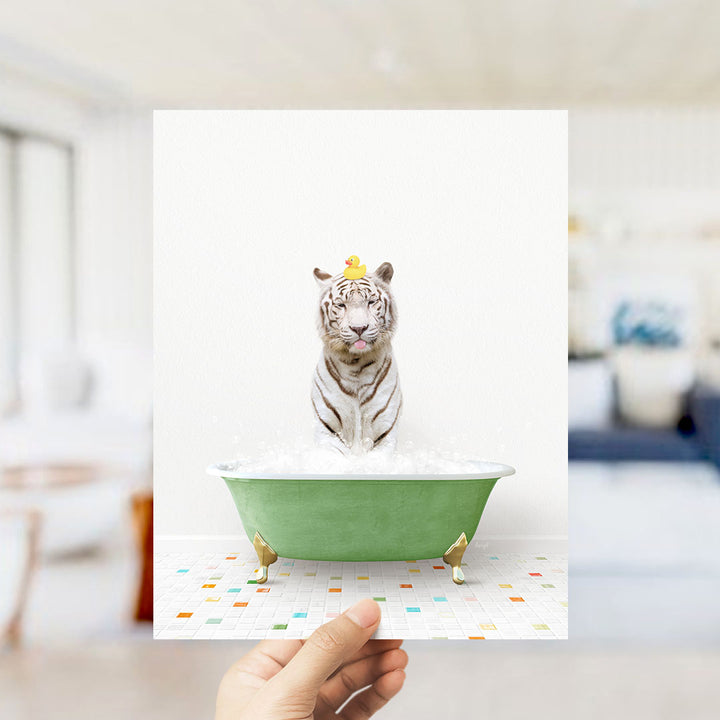 A white tiger is sitting in a green bathtub filled with bubbles, with a yellow rubber duck perched on its head.