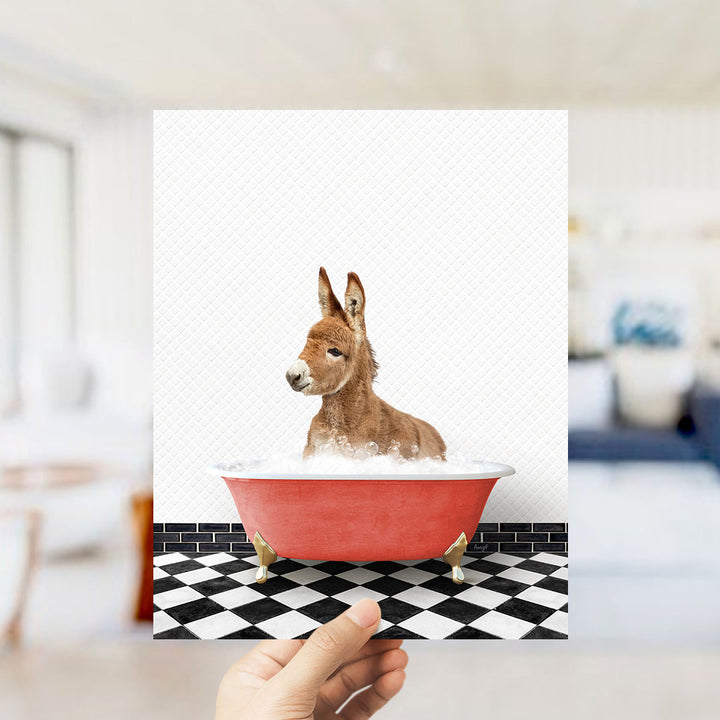 A donkey is sitting in a red bathtub filled with bubbles, with a person's hand holding up the image.