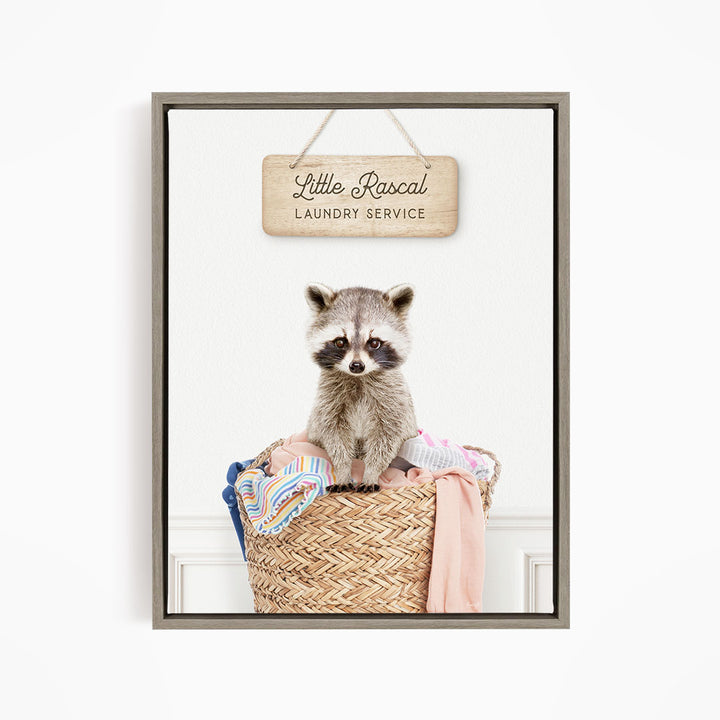 A raccoon sitting in a woven laundry basket, with a sign above that reads "Little Racal Laundry Service".