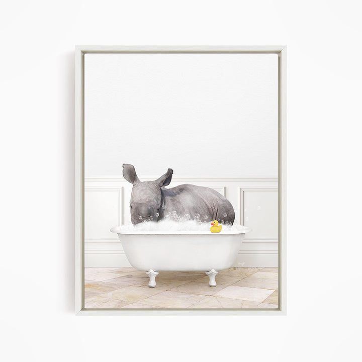 A rhinoceros is sitting in a white bathtub filled with water, with a yellow rubber duck floating in the water.