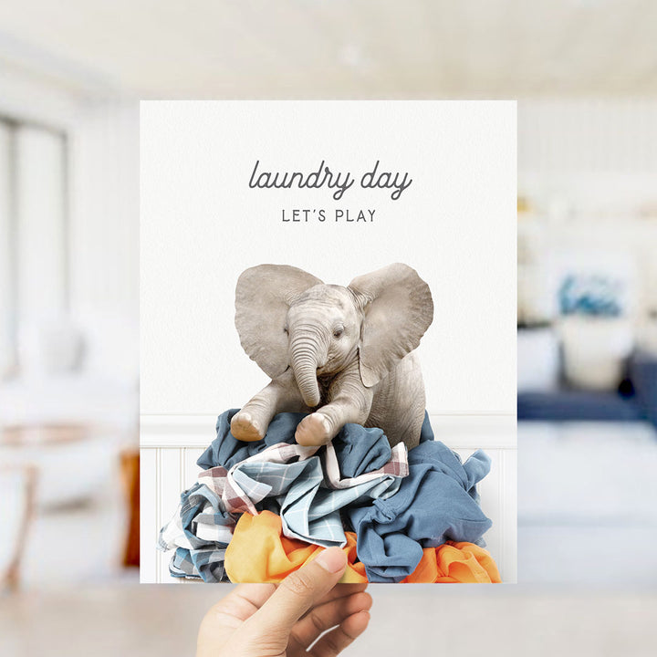 A hand holding a card with an image of a baby elephant sitting on a pile of laundry.