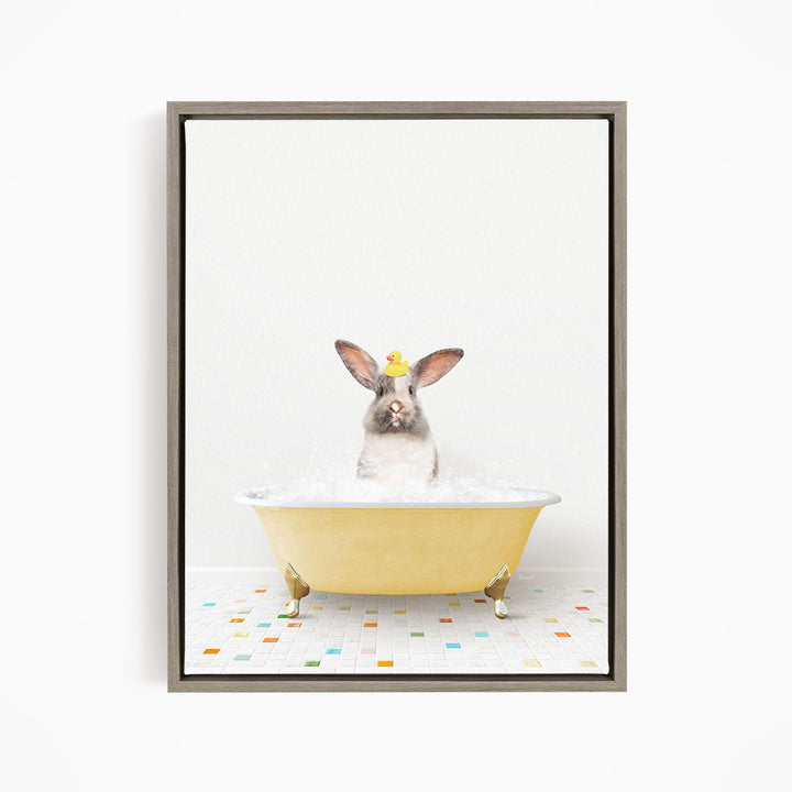A gray rabbit sitting in a yellow bathtub filled with bubbles, with a yellow rubber duck floating on the water.