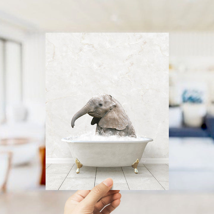 A hand holds up a framed image of a baby elephant sitting in a bathtub filled with water, creating a whimsical and playful scene.
