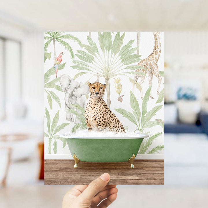 A hand holds up a framed print featuring a cheetah sitting in a green bathtub surrounded by tropical foliage, including a giraffe and an elephant.