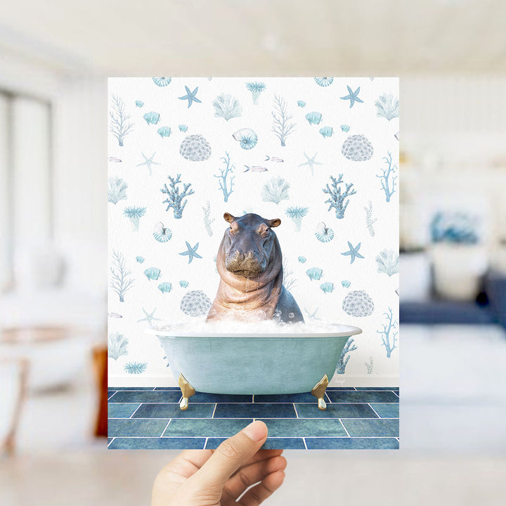 A hand is holding up a print featuring a hippopotamus sitting in a bathtub filled with bubbles, surrounded by a pattern of seashells, starfish, and other marine life.