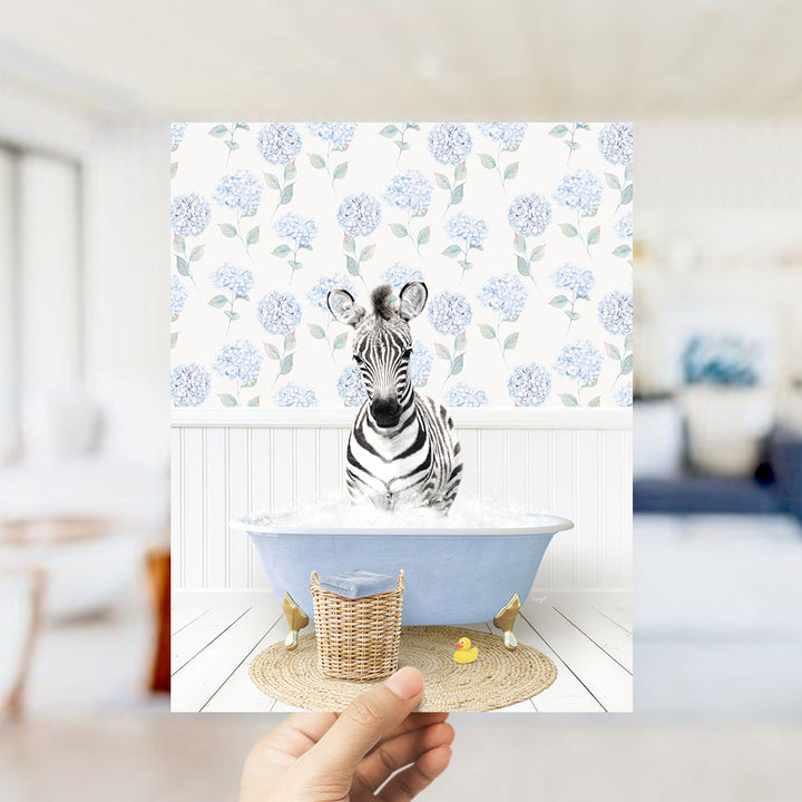 A zebra sitting in a blue bathtub filled with water, surrounded by a wicker basket and a rubber duck.