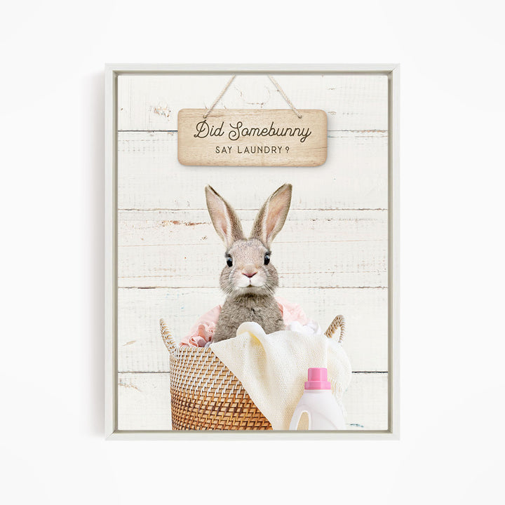 A cute rabbit sitting in a basket filled with laundry, with a sign above that says "Did Somebunny Sat Laundry?".